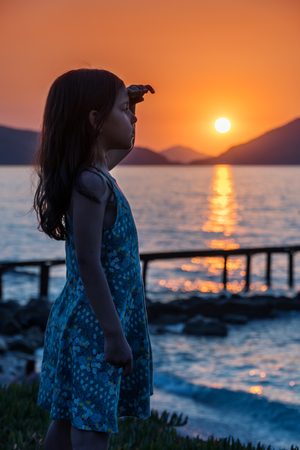 Little girl is enjoying sunset at the sea coast. Girl's silhouette at the sun setting.の写真素材