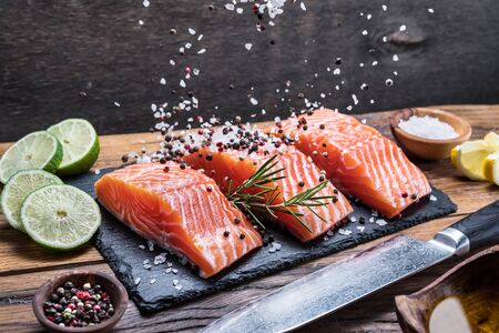 Fresh salmon fillets on black cutting board with herbs and spices.の写真素材