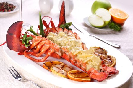 Baked lobster with applesauce and grilled bbq fruit on a white plate in a restaurant.の写真素材