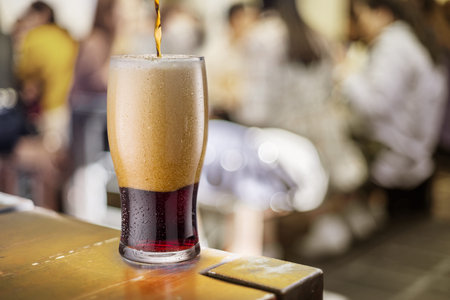 Pouring black beer into a glass at a counter in a pub. Behind the blurred pubs background.