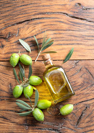 Green natural olives with bottle of olive oil on a vintage old wooden table.の写真素材