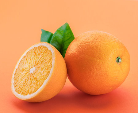 Orange fruit with orange slices and leaves isolated on orange background.