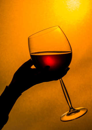 Drinking the red wine at the sunset. Woman hand holding a glass of red wine.の写真素材