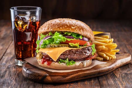 Delicious hamburger with cola and potato fries on a wooden table with a dark brown background behind. Fast food concept.の写真素材