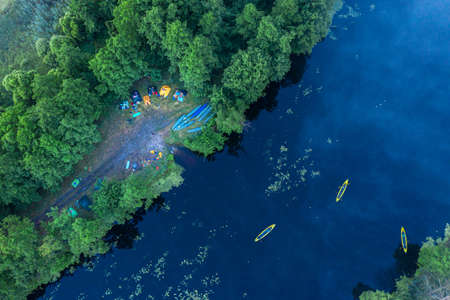Canoes on the calm river and camp on the bank of the river. Aerial top view. Beautiful picture of river and green banks of the river in the summer morning day.の写真素材