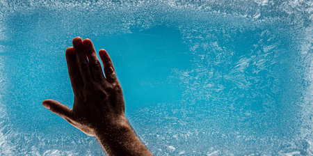 Frost patterns on frozen winter window as a symbol of Christmas wonder. Man's hand wipes the center of the window from frosty patterns. Christmas or New year background.の写真素材