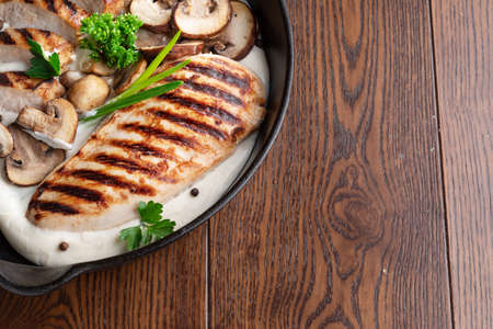 Roasted chicken fillet and mushrooms with herb in the frying pan on the wooden table close-up.の写真素材