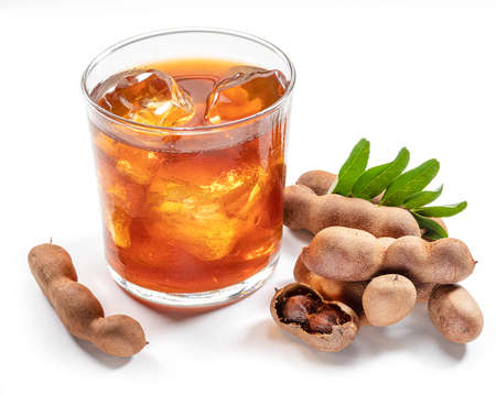 Glass of cool refreshing tamarind drink and some tamarind fruit on white background.の写真素材