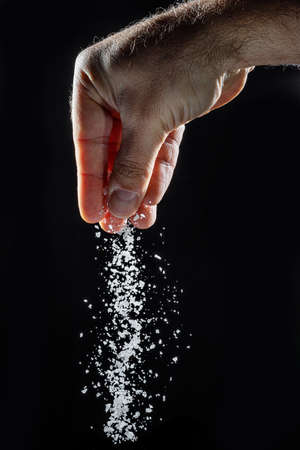 Male hand sprinkling edible salt at black background.の写真素材