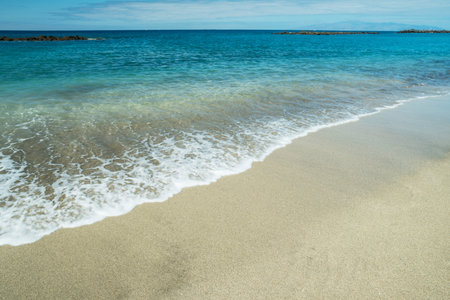 Ocean foam covering beautiful long sandy beach.