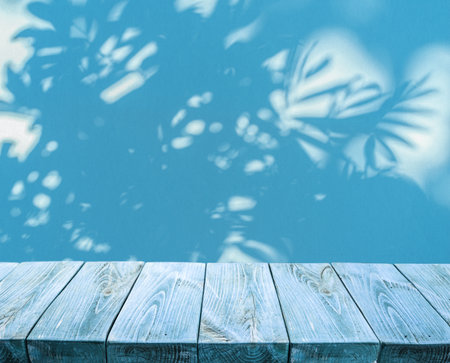 Blue empty plank table top and blue stucco pattern wall with leaf shadows. Place for your product display.の写真素材