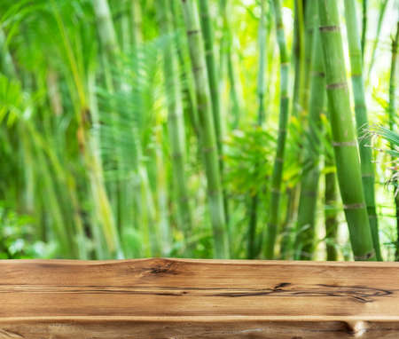 Empty wooden board or table top and blurred green bamboo culms. Place for your product display.の写真素材
