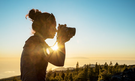 Silhouette woman with camera. Woman takes photo of La Gomera Island in the rays of the setting sun. Tenerife Island.の写真素材