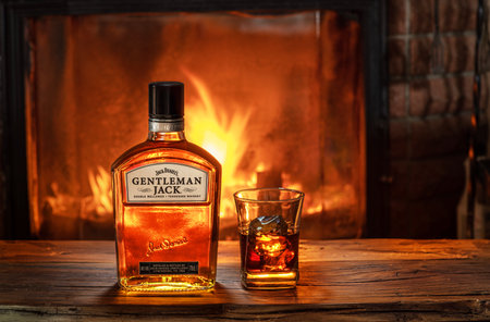 Kyiv, Ukraine â March 25, 2021. Bottle of Gentleman Jack Daniels whiskey with a glass of whiskey on an old wooden table in front of a burning fireplace, vintage style.のeditorial素材