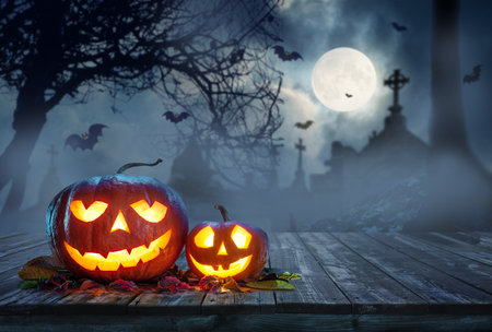 Carved lightening pumpkins for Halloween jack-o'-lanterns with scary smiles to ward of evil spirits on mystery night cemetery background. Halloween background.の写真素材