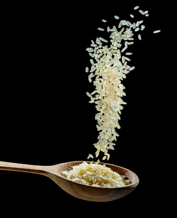 White rice grains falling down into the spoon at black background. Popular food and main ingredient of risotto and pilau.の写真素材