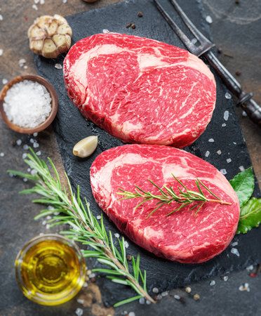 Raw ribeye steaks with rosemary and other seasoning on gray tray. top view.の写真素材