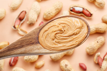 Wooden spoon with peanut butter. Peanuts lay on beige at the background. top view.の写真素材