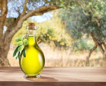 Bottle of craft farm olive oil stands on a wooden table, behind is an olive garden in a slightly bokeh, sunny day.の写真素材