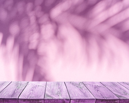 Blurred shadow of tropical palm leaves on pink wall and old planked table top in the foreground. summer concept.の写真素材