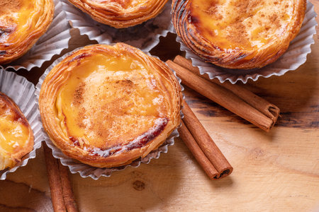 Pastel de nata tarts and cinnamon sticks on wooden tray. top view.