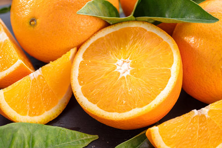 Ripe orange fruits with slices and orange tree leaves on a gray stone table.