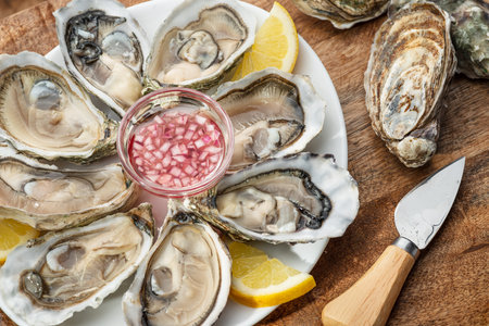 Opened raw oysters with sauce and lemon slices on plate on wooden table. Top view.の写真素材
