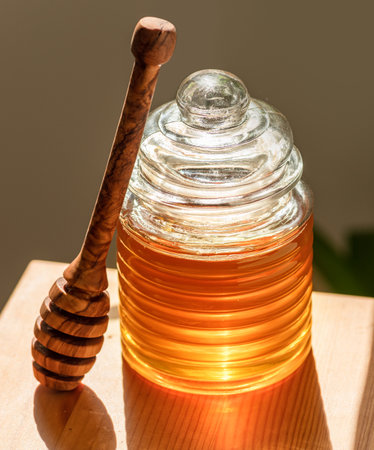 Natural organic honey in glass jar, wooden dripper spoon near it isolated on table.の写真素材