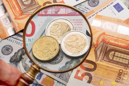 Business background from world famous currencies - paper banknotes and coins of euros and dollars. In the foreground, a man's hand holds a magnifying glass.の写真素材