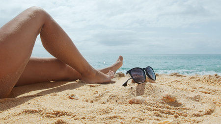 Woman sits on a sandy sea beach on a sunny summer day. Female legs in the frame.の写真素材