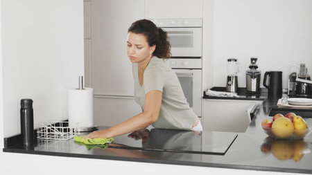 Woman is cleaning the kitchen countertop and electric stove or electric hob.