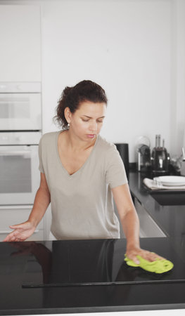 Woman is cleaning the kitchen countertop and electric stove or electric hob.
