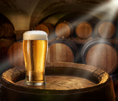 Glass of chilled beer on old wooden cask and wooden beer casks at the background.の写真素材