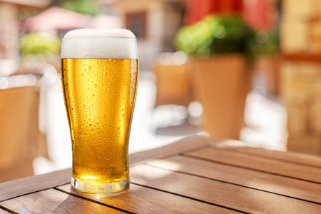 Glass of chilled beer on wooden table and blurred summer terrace at the background.の写真素材