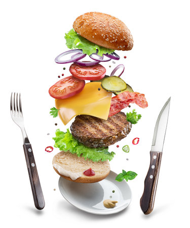 Cheeseburger ingredients with beef patty, vegetables and cheese floating in the air above a plate and cutlery next to it on a white background. File contains clipping paths.の写真素材