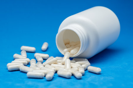 White capsules or tablets poured out of plastic bottle on a blue background. Concept of medicine, health care, food supplements and pharmaceutical treatment.の写真素材