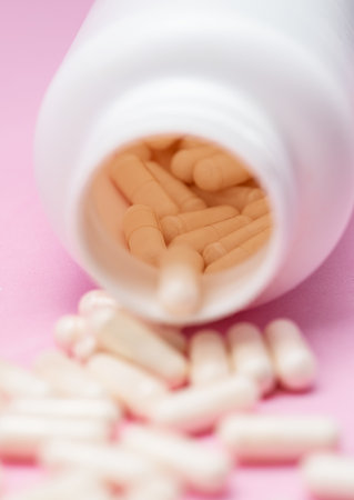 White capsules or tablets poured out of plastic bottle on pink background. Concept of medicine, health care, food supplements and pharmaceutical treatment.の写真素材