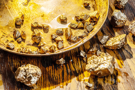 Gold nuggets on a brass plate on a wooden tabletop.の写真素材