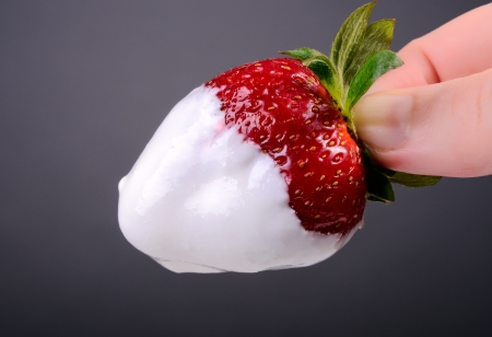 A hand is holding a strawberry in sour creamの写真素材