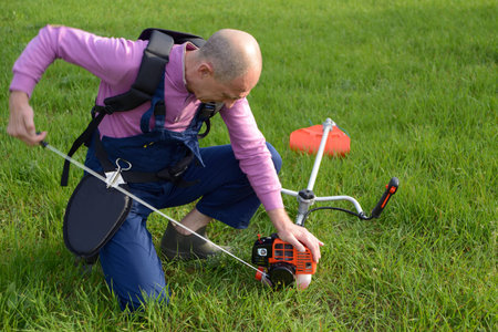 The man starts a weed trimmer on a lawn
