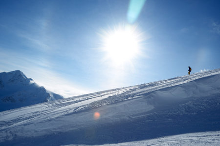 Skier going down the slope on a background of blue sky and mountainsの写真素材