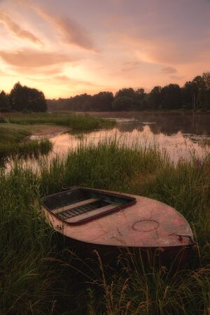 Boat in the grass by the river. Dawn over the river, image in the orange toning.の写真素材