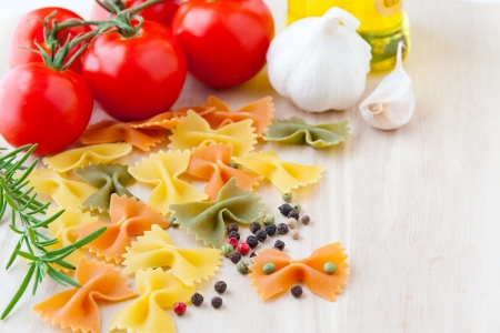 Ingredients for Italian cuisine  bow tie pasta, tomatoes, olive oil, rosemary, garlic and pepper  selective focusの写真素材