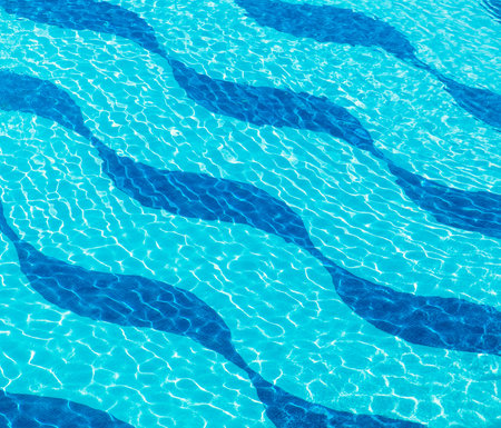 Resort swimming pool with wave pattern and  sunny reflections, blue water background texture.