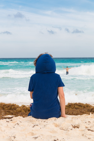 Woman sitting on the beach with sand and seaweeds, looking at the stormy ocean.の写真素材