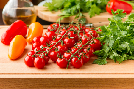 Tomatoes, mini bell peppers and parsley on wooden cutting board. Ingredients for fresh salad, healthy food.の写真素材