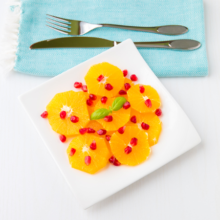 Fresh citrus salad with oranges and pomegranate seeds on white plate with silverware.の写真素材
