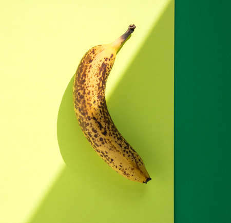 Over ripe banana with dark spots on hard light with shadows,  yellow background with green border.の写真素材