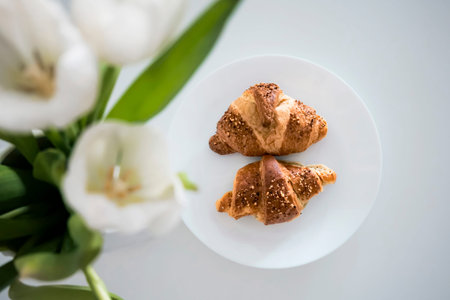 Tho croissants on a plate with white tulips in a vase in the foregroundの写真素材