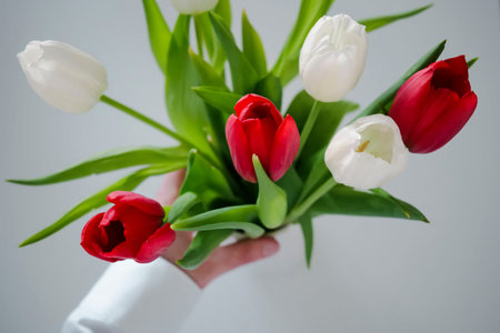 Hand holding a white ribbed vase with a colourful bouquet of tulipsの写真素材